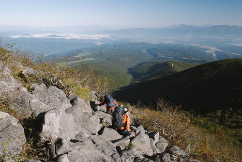 蓼科山の険しい岩場を進む登山者と雄大な山並み