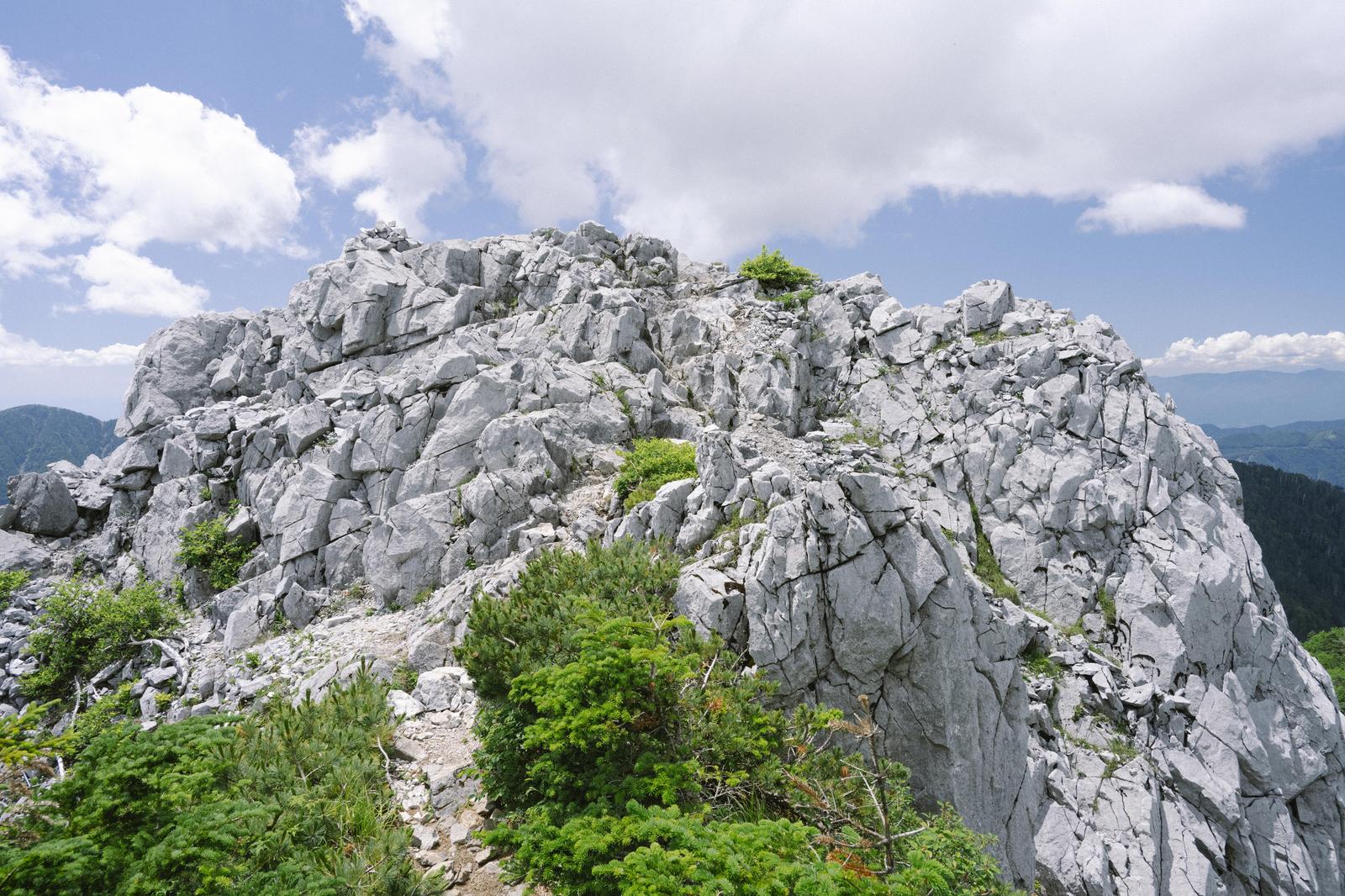 光岳の白い岩峰と緑の植生、青空の山岳風景