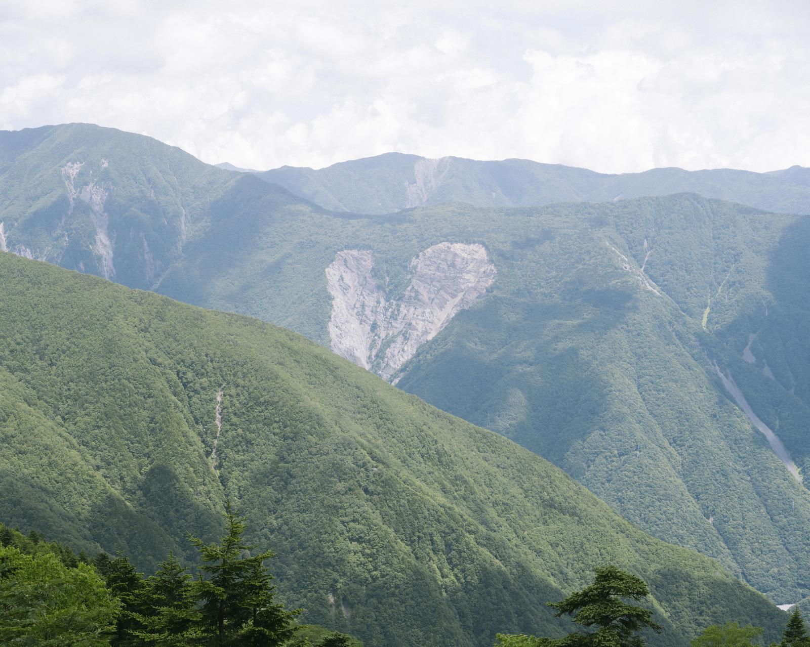 深い渓谷を背景に、緑の斜面に白いハート形の岩肌が見える山岳風景
