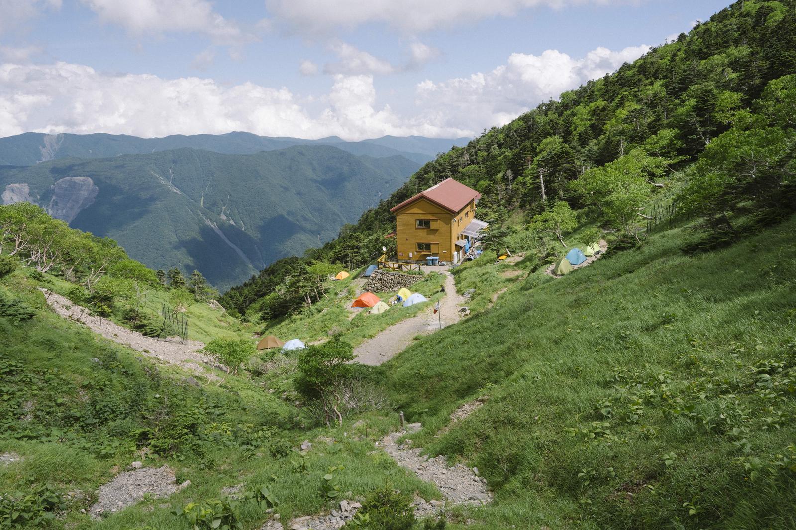 光岳の山腹に建つ黄色い茶臼小屋と複数のテントが張られたキャンプ場