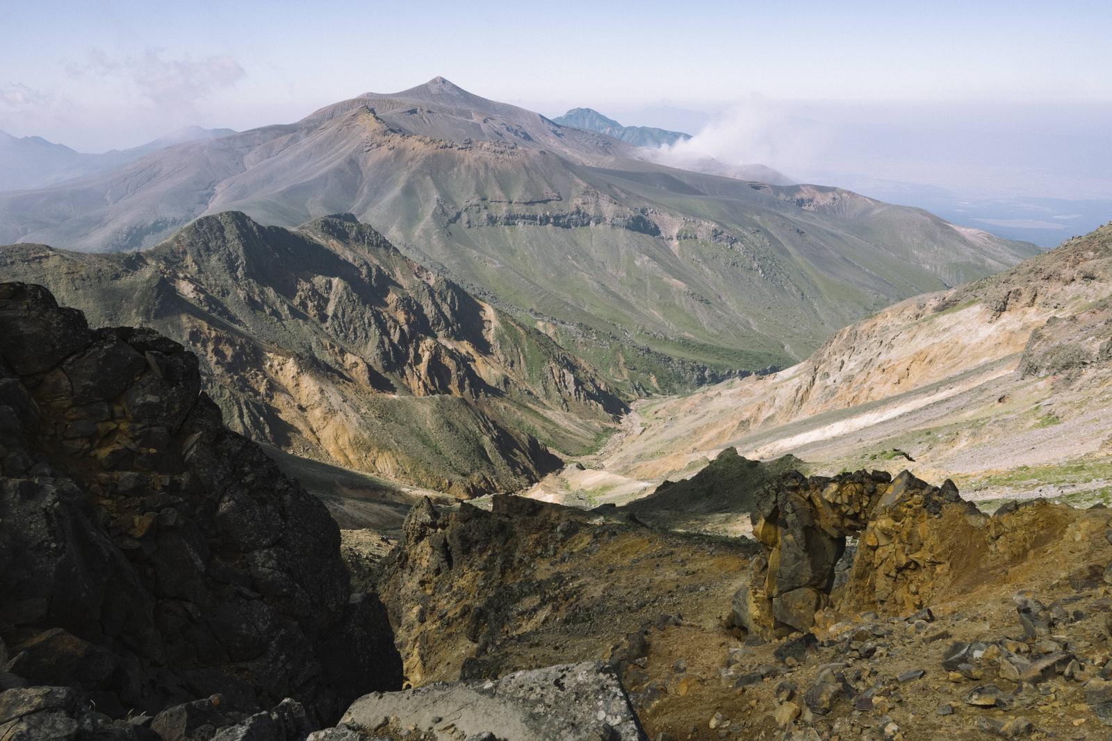 美瑛岳の火口から見た十勝岳の山頂。手前に露出した岩場と土砂、奥に円錐状の十勝岳が見える