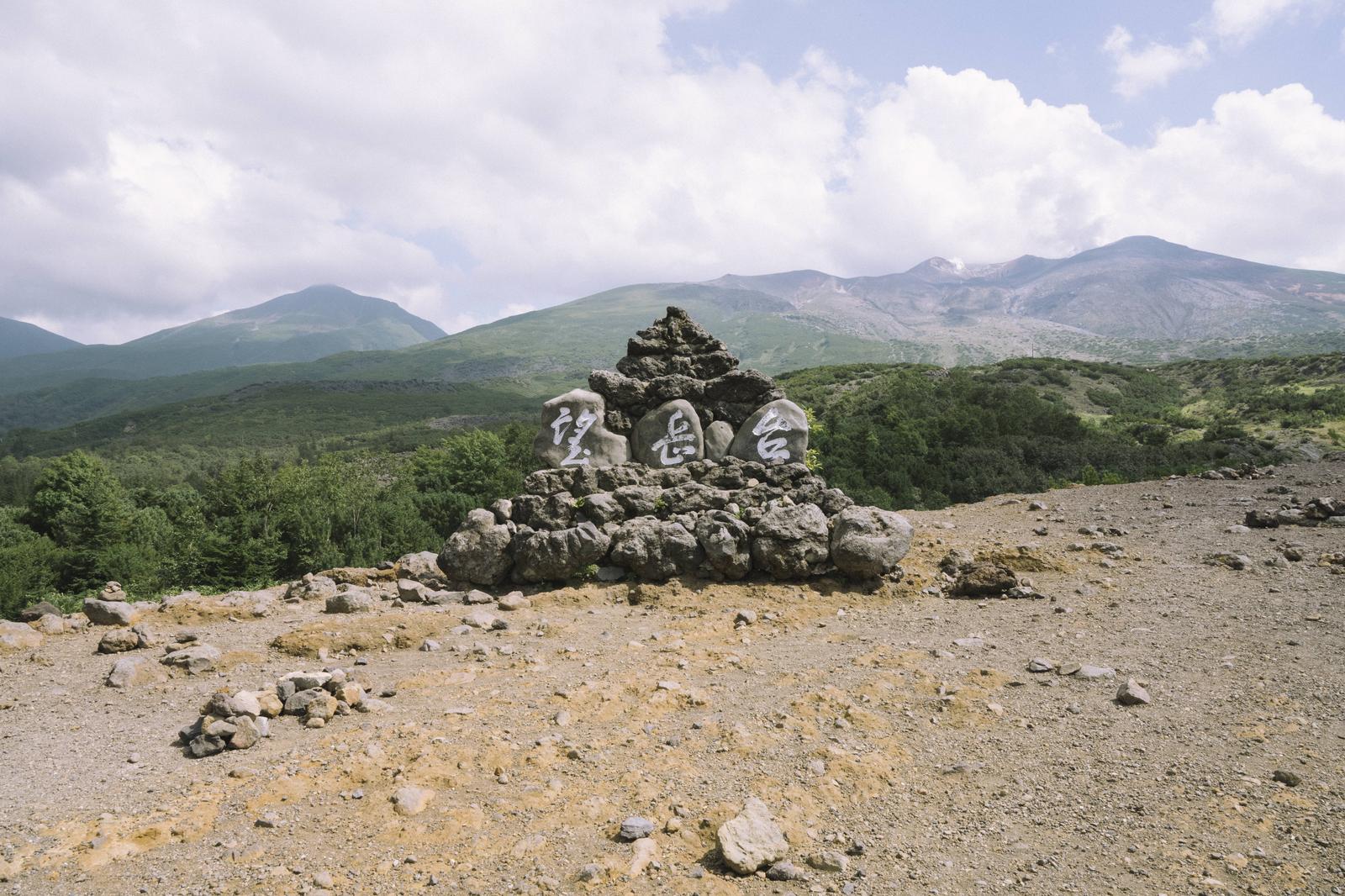 十勝岳の登山口にある石碑と奥に連なる山々の風景