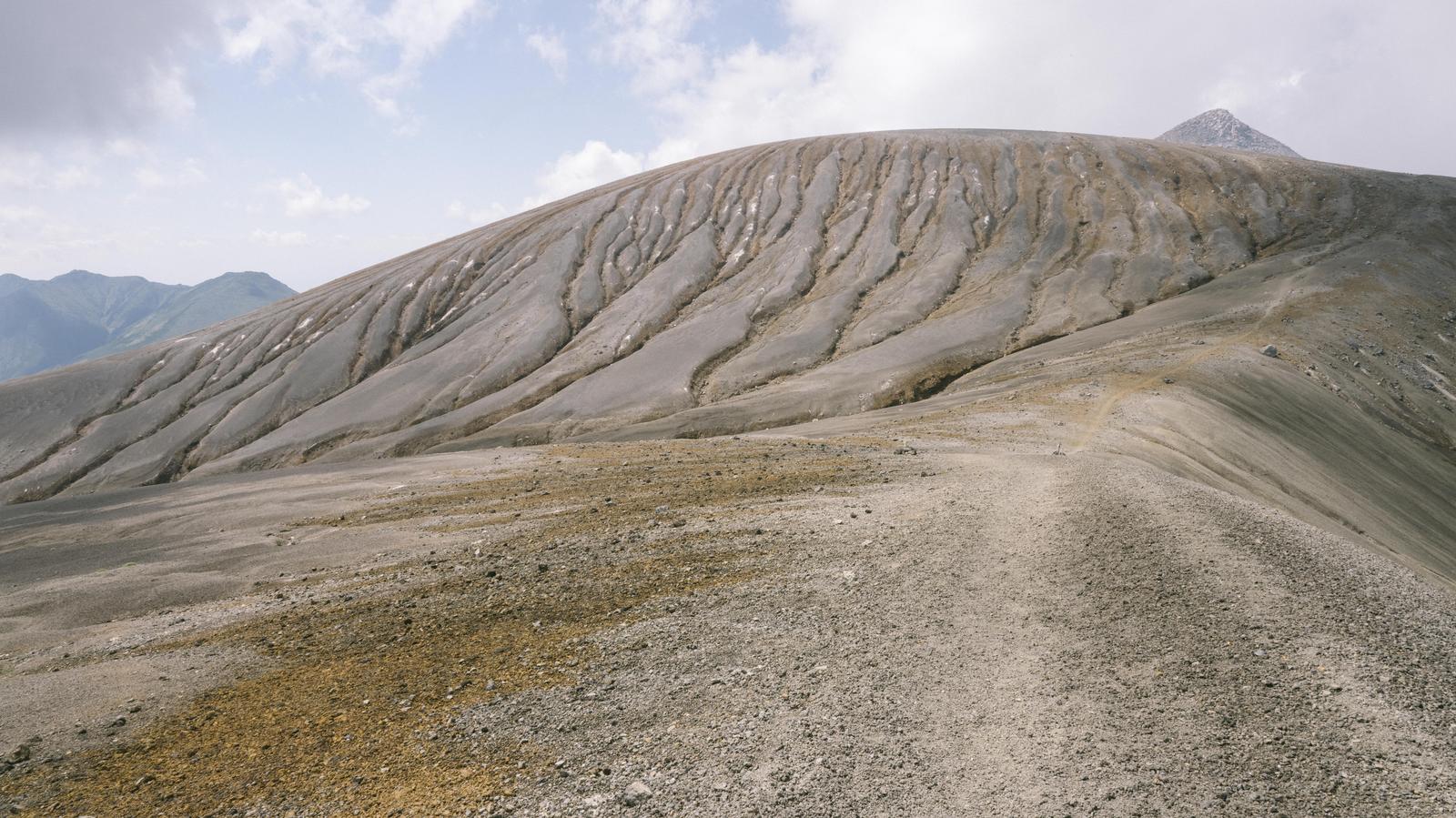 十勝岳の登山道沿いで雨裂が走る灰色の平ヶ岳台地と連なる山々