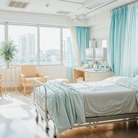 朝日が差し込む水色カーテンの清潔な病院個室の写真