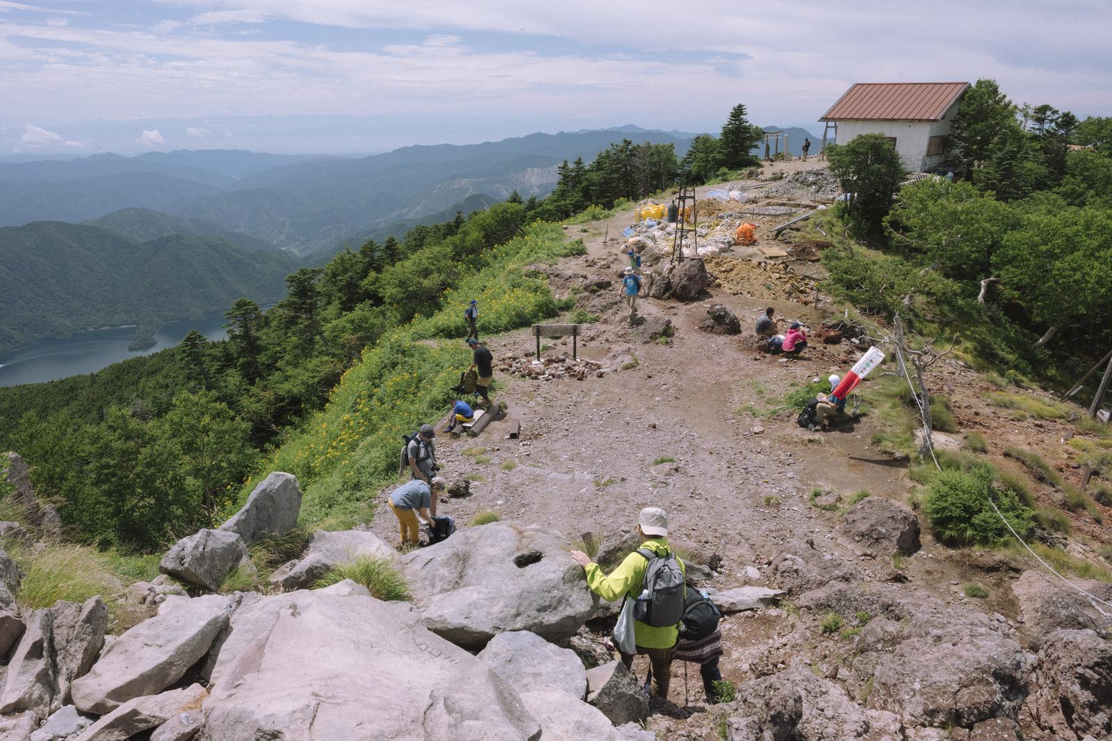 日本百名山・男体山の山頂で立ち止まる複数の登山者と白い山小屋