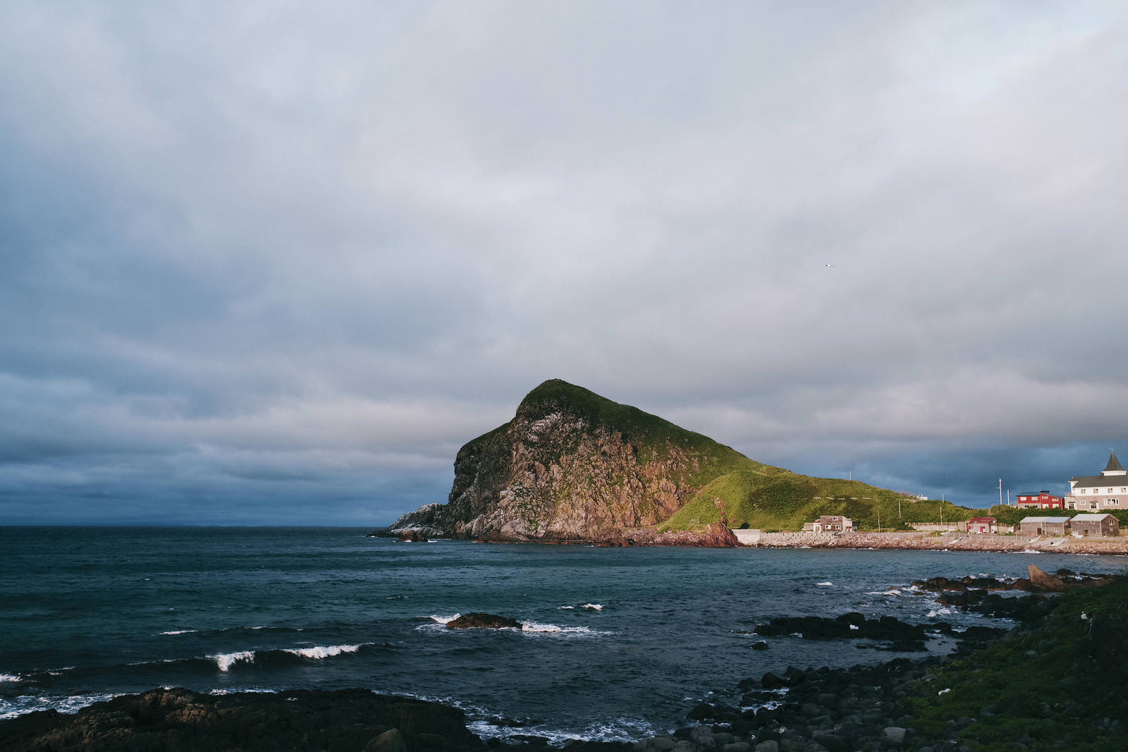 利尻岳とペシ岬の北海道の海岸風景。緑の山と海、赤い建物が見える