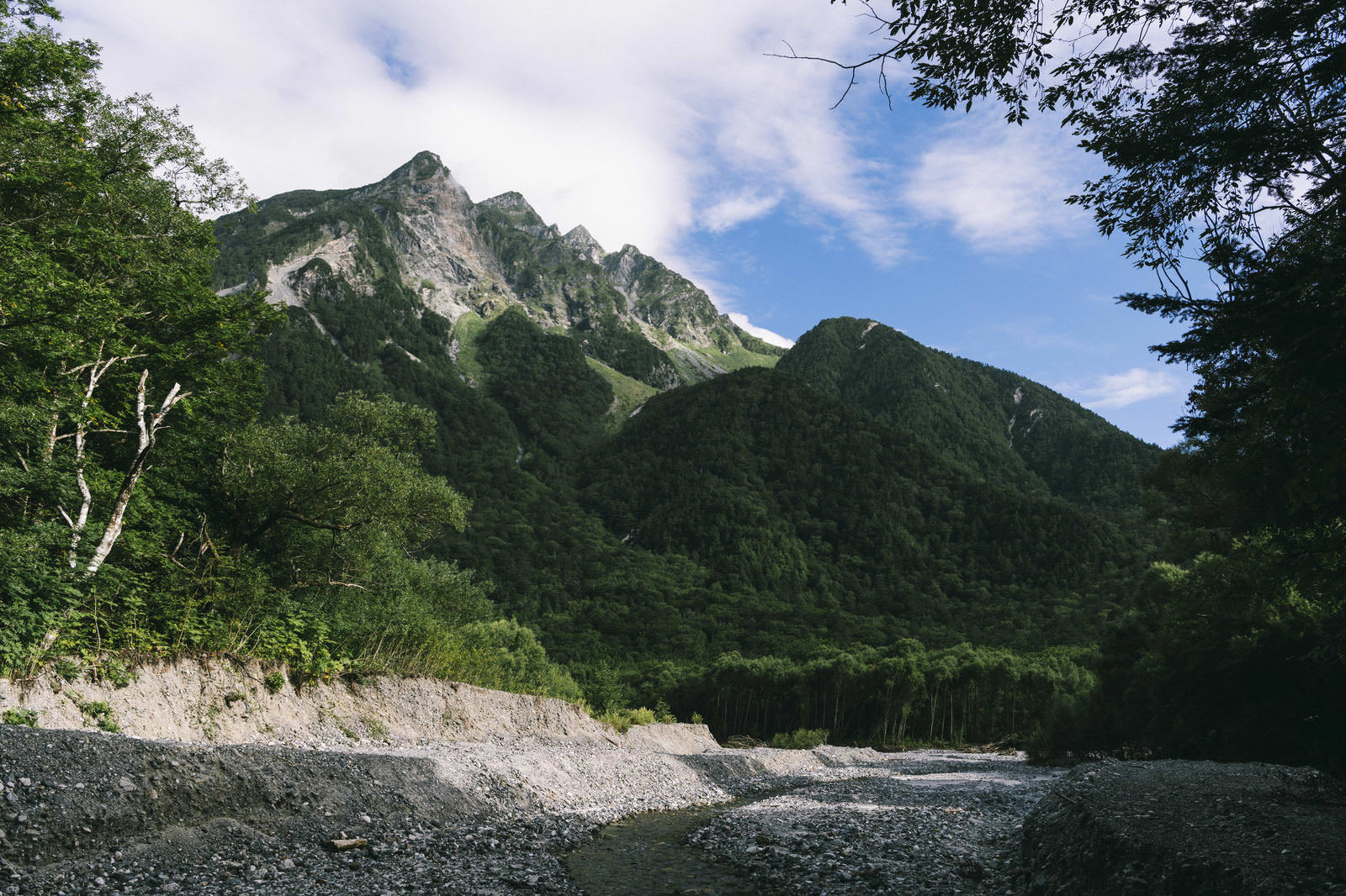 梓川の河原から見上げる、露出した岩肌の奥穂高岳と周辺の山々