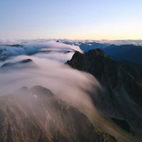 滝雲が流れ落ちる奥穂高岳の山並み、雲海と朝焼けの絶景の写真
