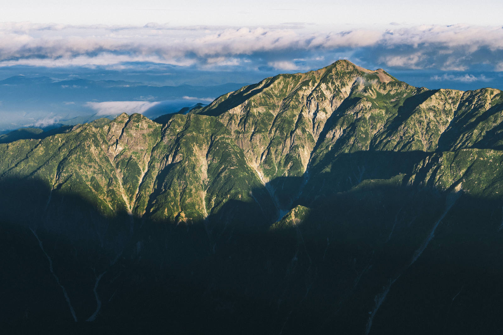奥穂高岳付近の笠ヶ岳など山々が連なる山脈の風景。緑の森と岩肌、青空の景観