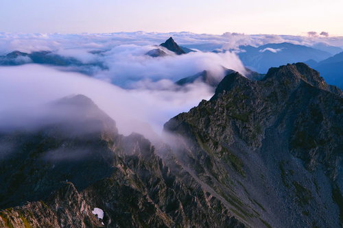雲が流れる奥穂高岳の岩の稜線、朝焼けに染まる北アルプスの山々