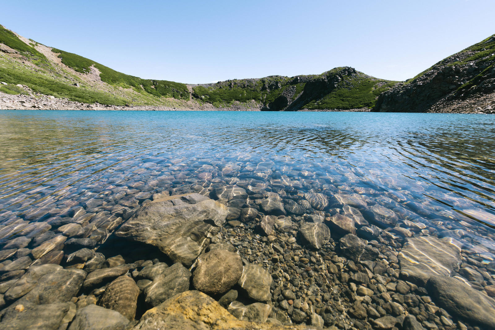 御嶽山の三ノ池。透き通った青い湖水に岩が見える湖面と、周囲の緑の山々