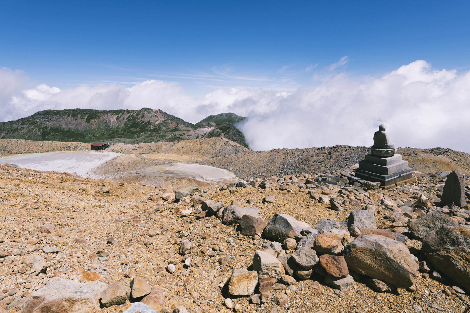 御嶽山の二ノ池畔に立つ石積みの仏像と雲海に包まれた山々