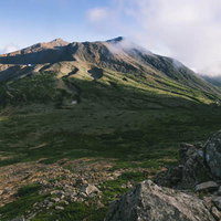 夕日に照らされる御嶽山の剣ヶ峰方面、火山礫の山肌と緑の草地の写真