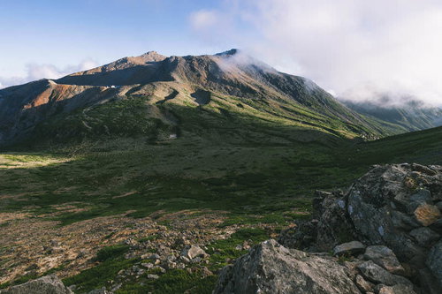夕日に照らされる御嶽山の剣ヶ峰方面、火山礫の山肌と緑の草地