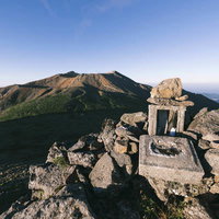 御嶽山の朝、山頂の石造りの祠と遠景の山々の写真