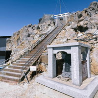 御嶽山剣ヶ峰入口の石造鳥居と慰霊碑、登山道の階段の写真