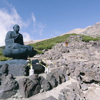 日本百名山・御嶽山の登山道に立つ銅像と山頂からの景観の写真