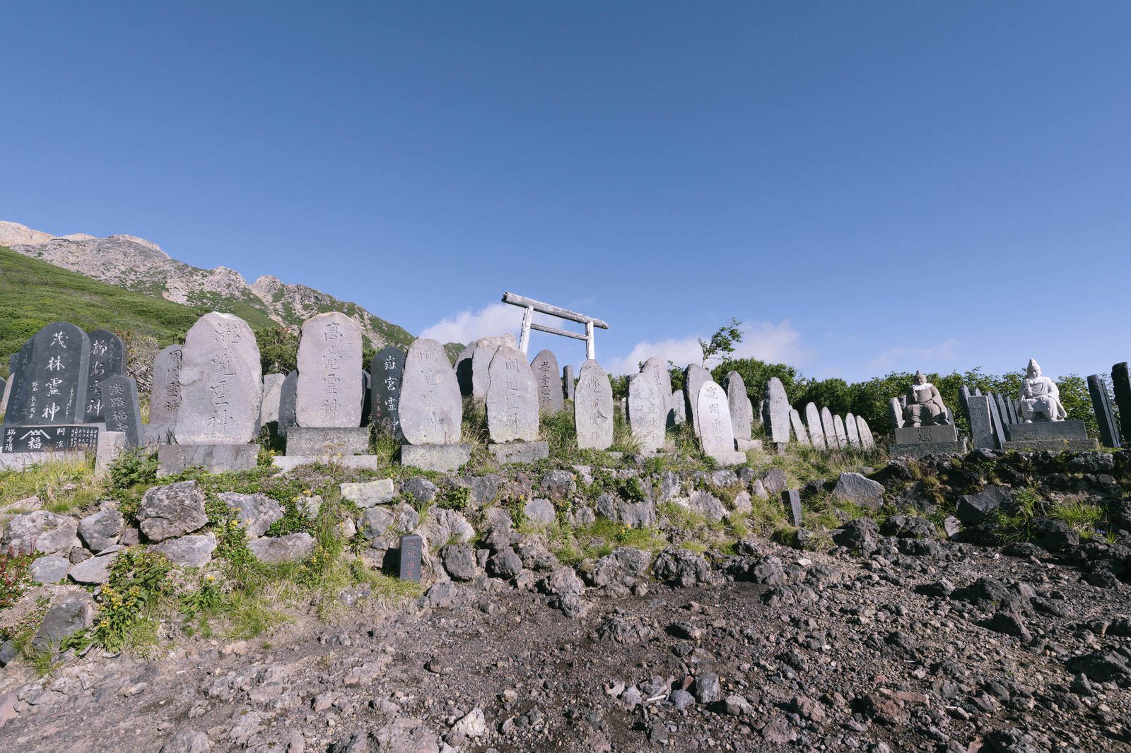 御嶽山の登山道脇に立ち並ぶ複数の石碑と青空の風景