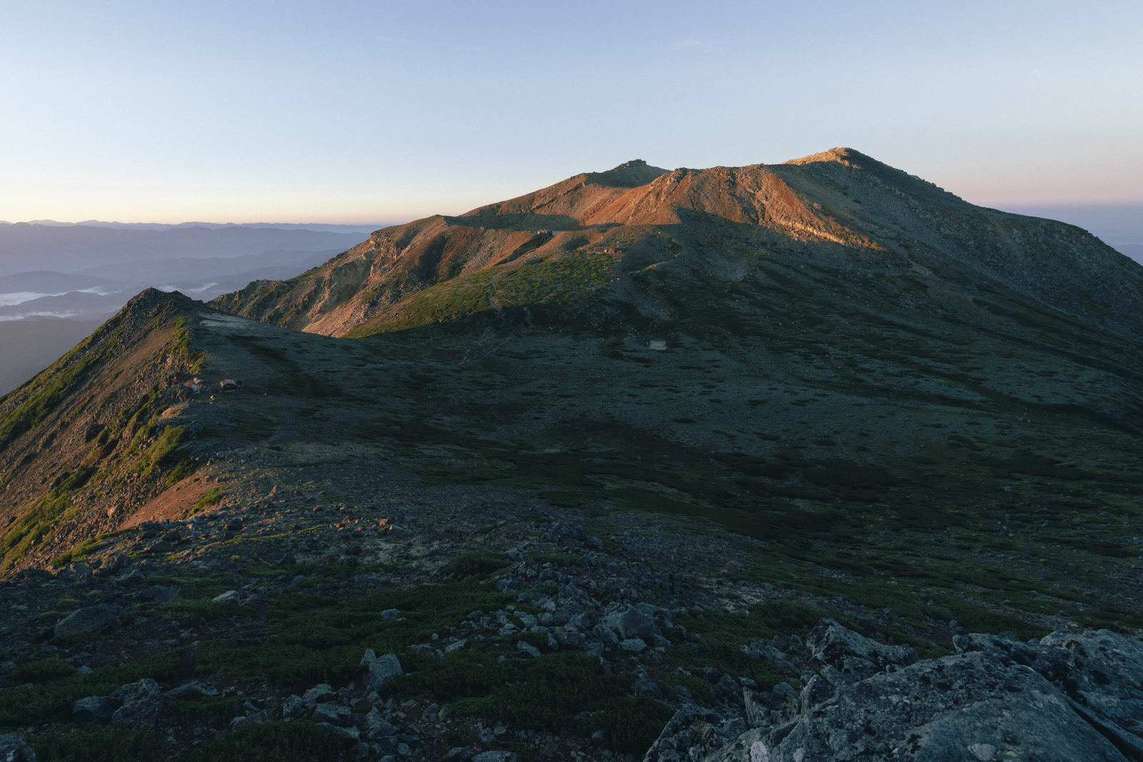朝日でオレンジ色に照らされた御嶽山の剣ヶ峰とザレた稜線