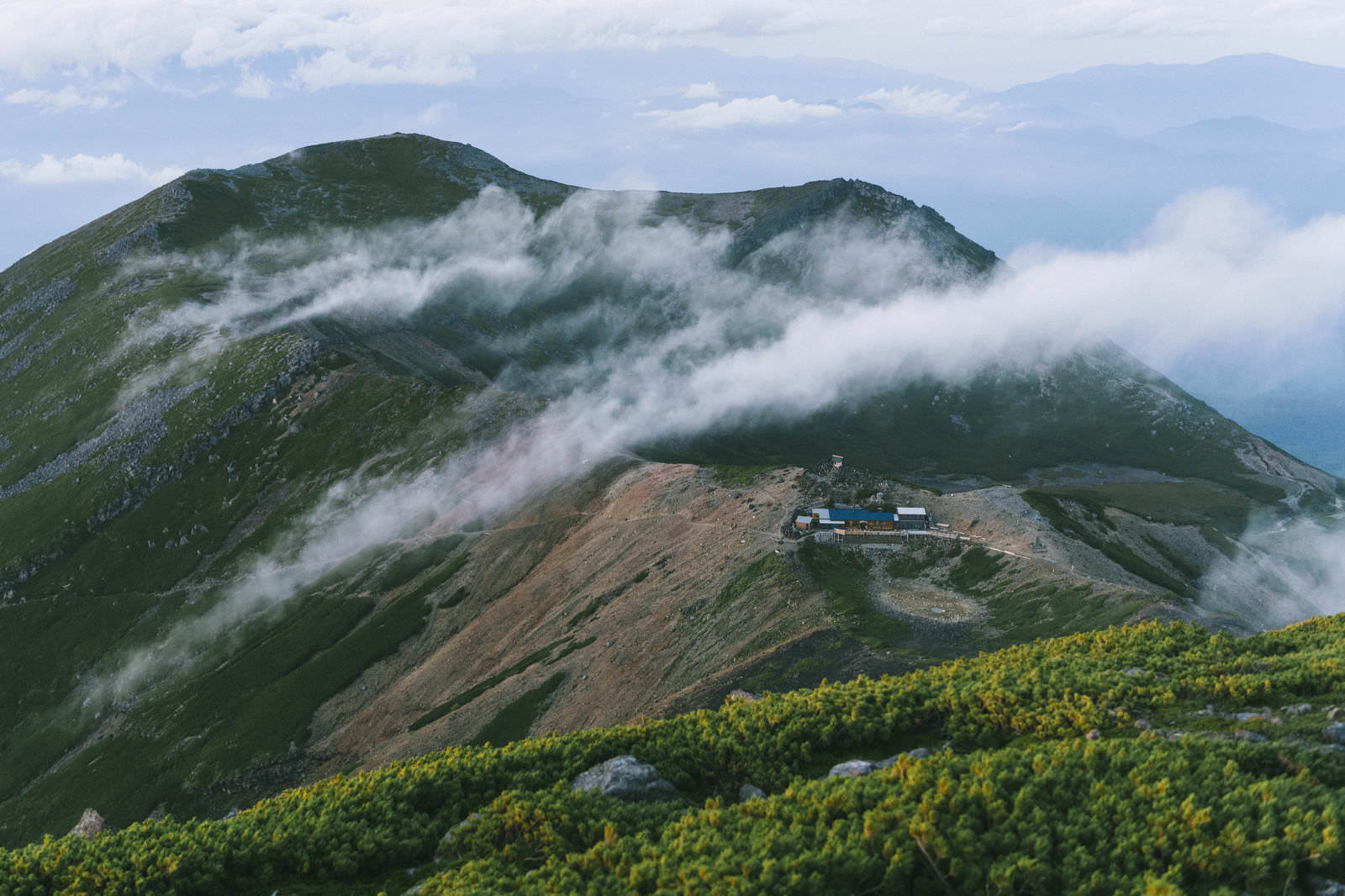 雲に包まれた緑の山肌に建つ五ノ池小屋と継子岳の山岳風景