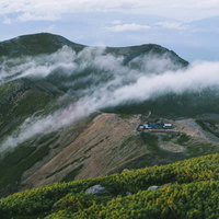 流れる雲に包まれる御嶽山の五ノ池小屋と継子岳の写真