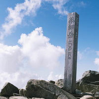 日本百名山の薬師岳山頂に立つ石製の山頂標と青空の写真