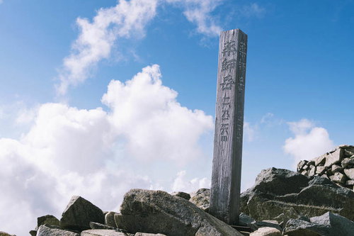 日本百名山の薬師岳山頂に立つ石製の山頂標と青空