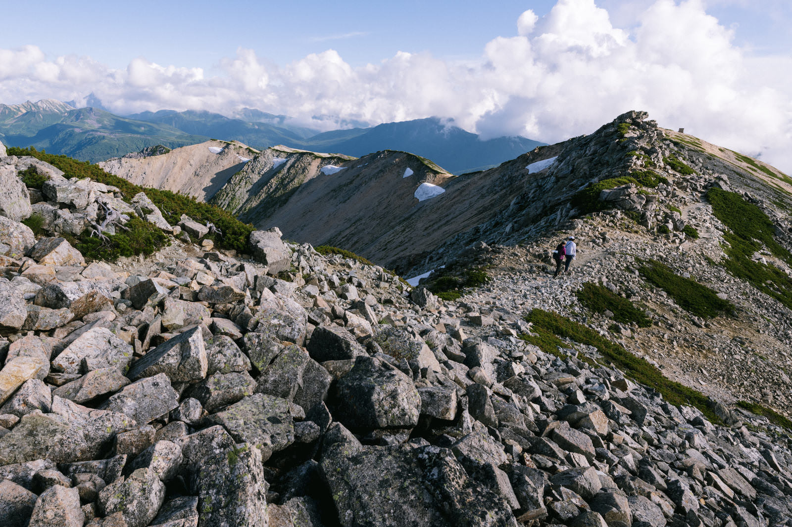 薬師岳の山頂稜線で歩くハイカー。白い岩場と遠方の連峰が見える