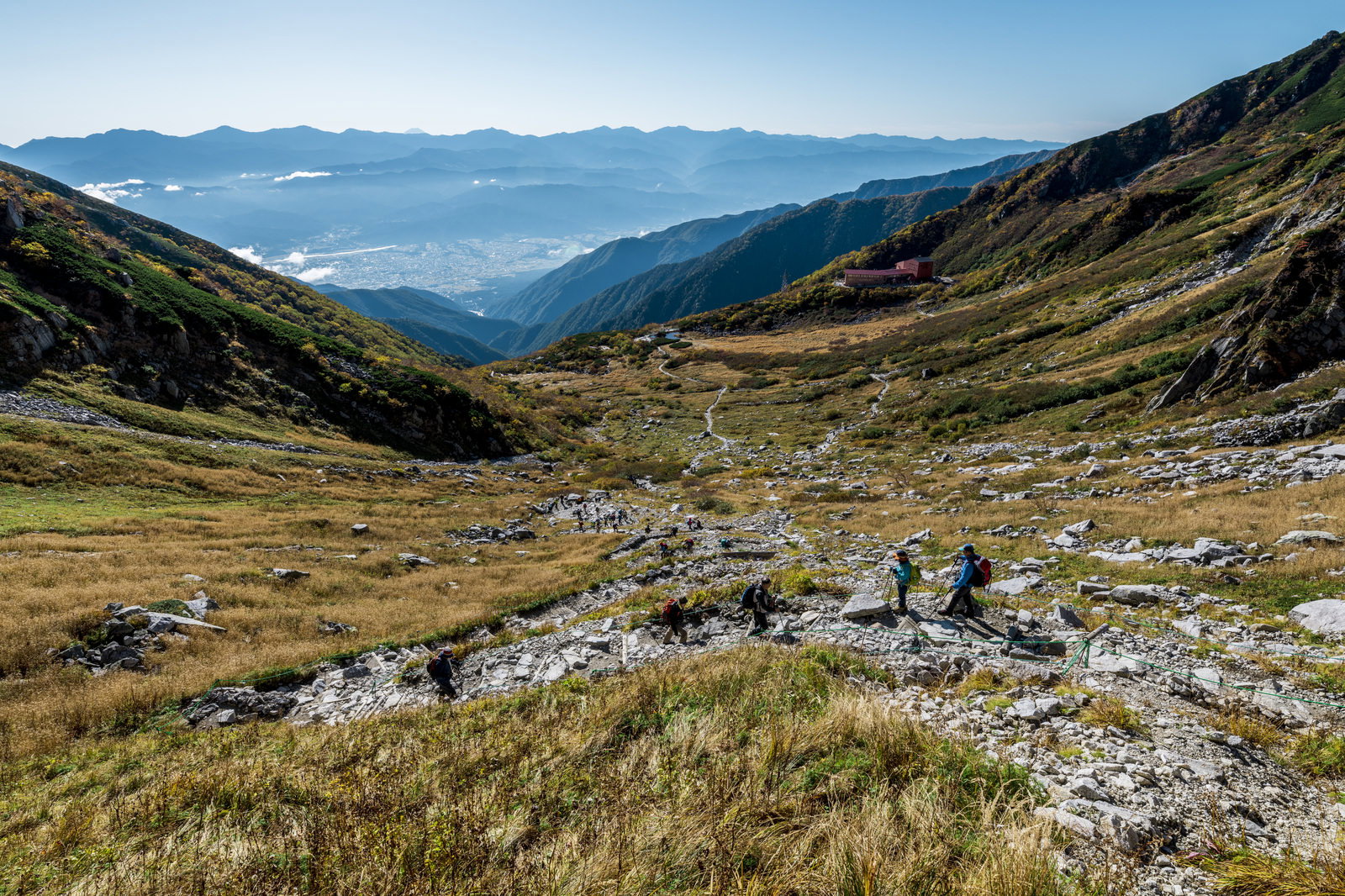 紅葉の千畳敷カールの登山道を歩く登山者と、眼下に広がる雲海と山並み