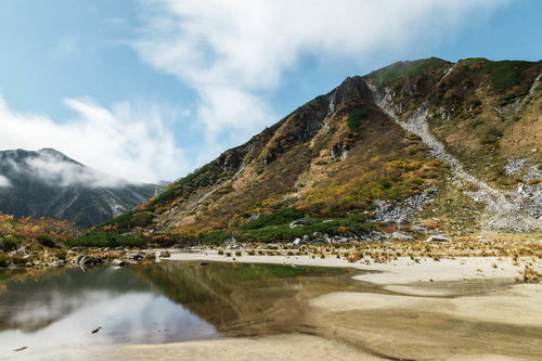 秋の濃ヶ池に映る雲と紅葉した木曽駒ヶ岳の山岳風景