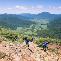 至仏山の岩場の登山道を歩く登山者と眼下の尾瀬の写真