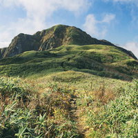笹原の向こうに堂々と見える雨飾山の山容と登山道の風景の写真