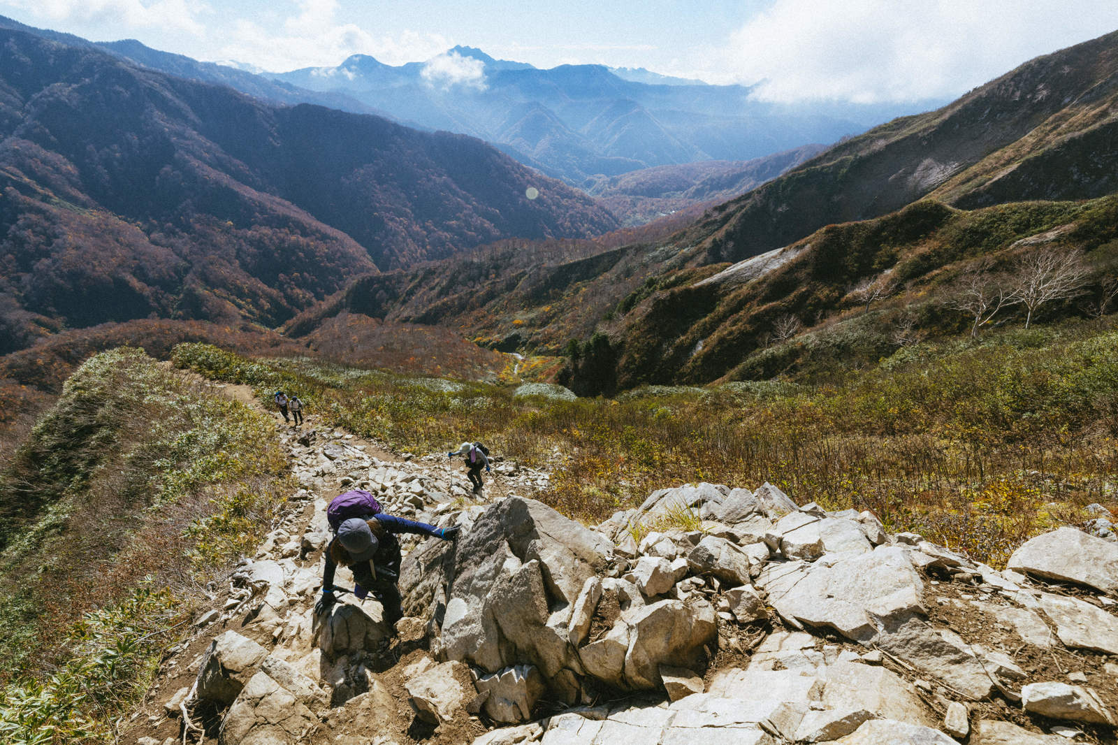 荒菅沢登山道を歩く登山者と雨飾山の紅葉した山腹風景