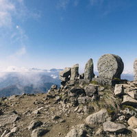 日本百名山・雨飾山山頂の岩場に立つ石仏と青空の写真