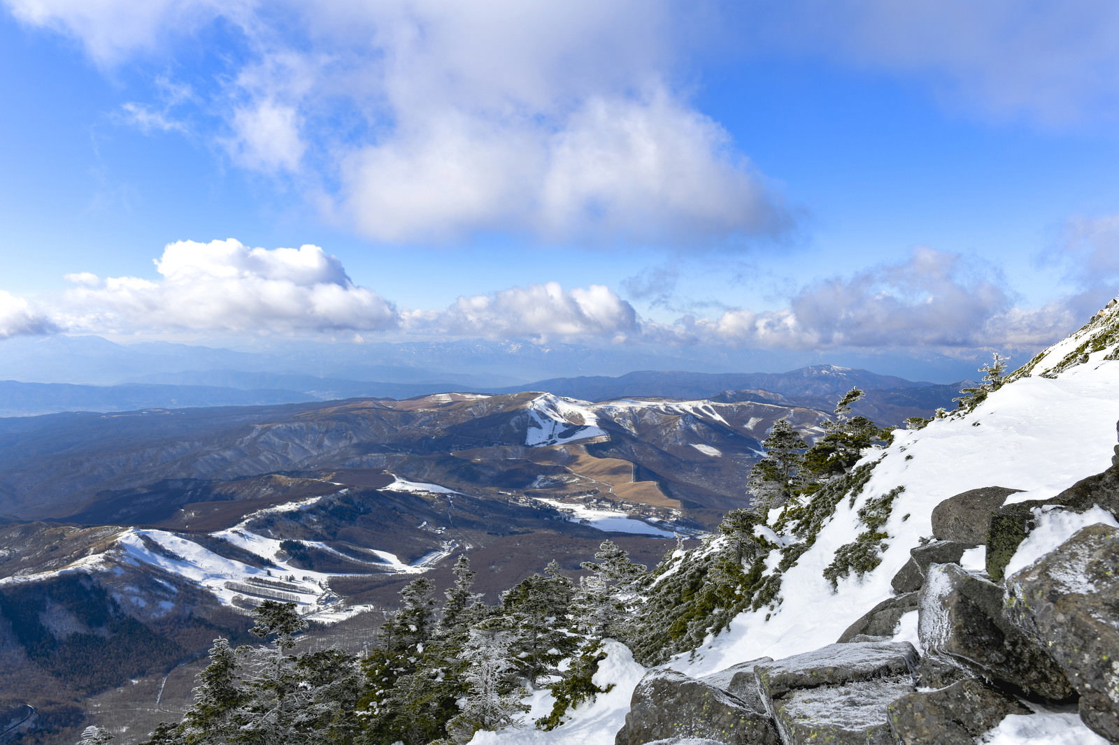 蓼科山から霧ヶ峰方面を望む雪景色、青空と白い雲が広がる冬の山岳風景