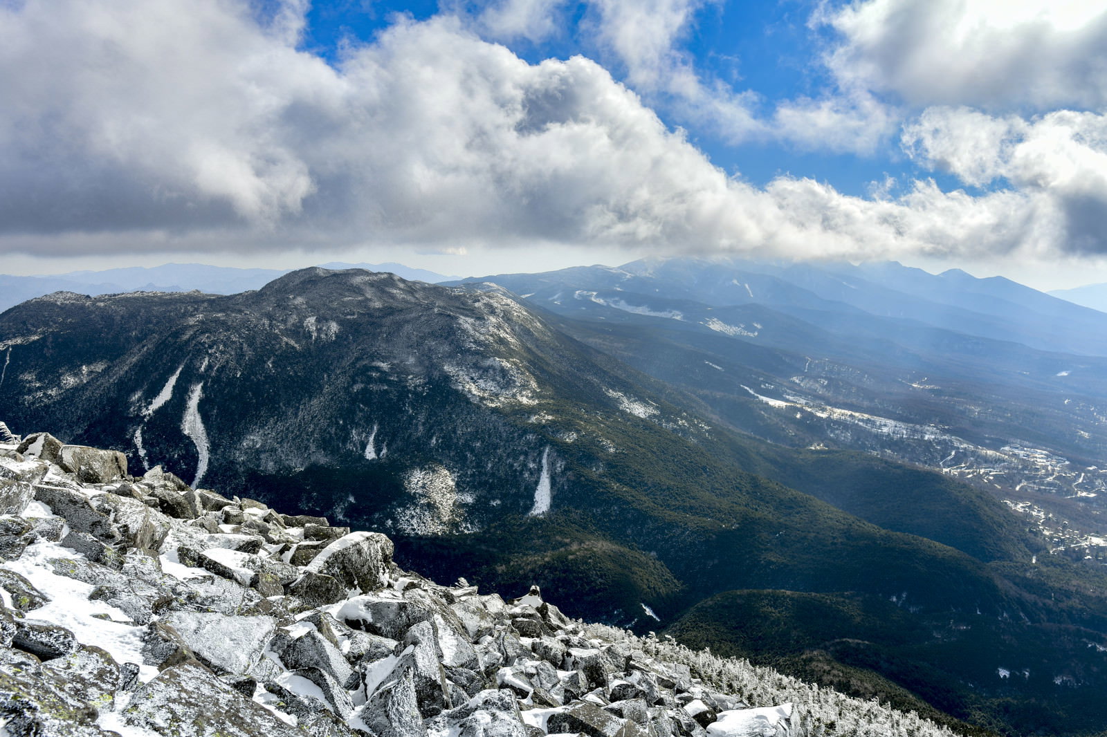 蓼科山山頂から望む雪化粧した北八ヶ岳の山並みと青空に浮かぶ白い雲