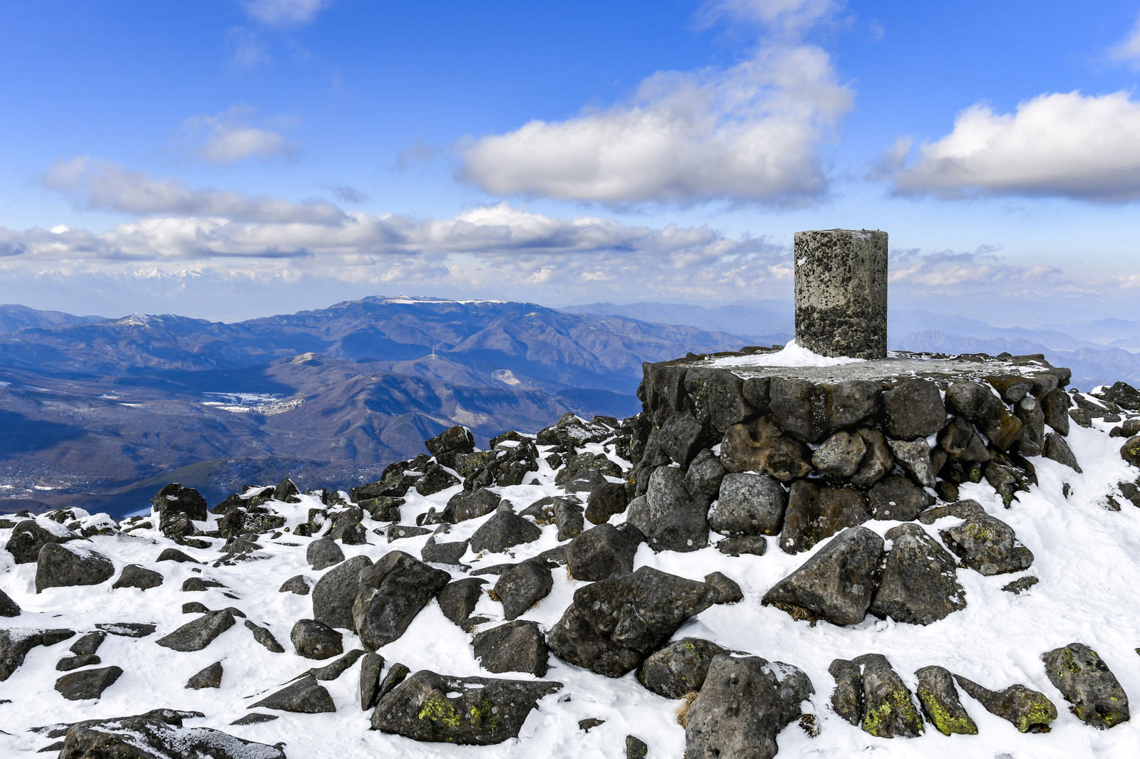 雪の蓼科山山頂に立つ石碑と美ヶ原方面の山々を望む冬景色