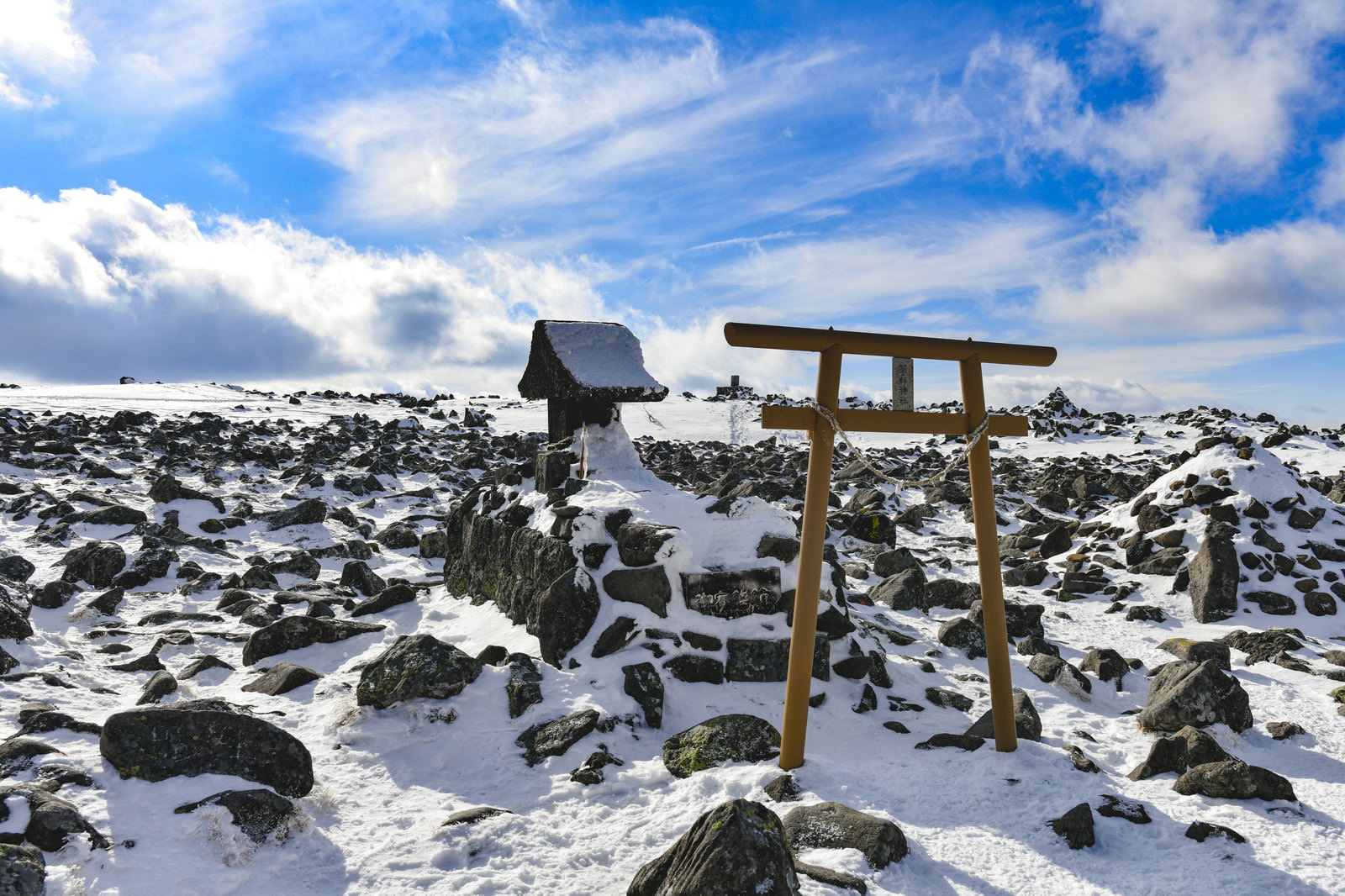 雪化粧した蓼科山山頂に立つ木造の社と鳥居、青空と雲が広がる
