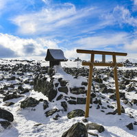 蓼科山山頂の雪に覆われた社と鳥居、残雪と岩場の風景の写真