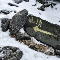 雪の岩場に立つ蓼科山山頂へといざなう標識の写真