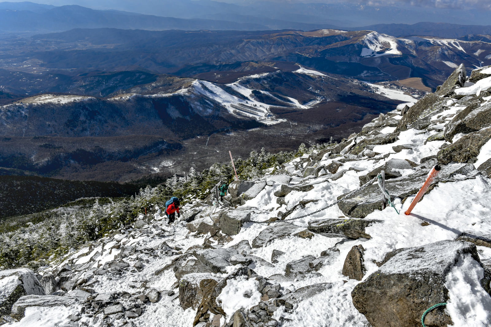 雪に覆われた蓼科山の岩場を山頂に向かって登る登山者