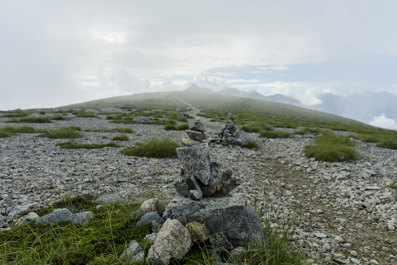 石を積み上げたケルンの向こうにガスがかかった槍ヶ岳が見える山岳風景