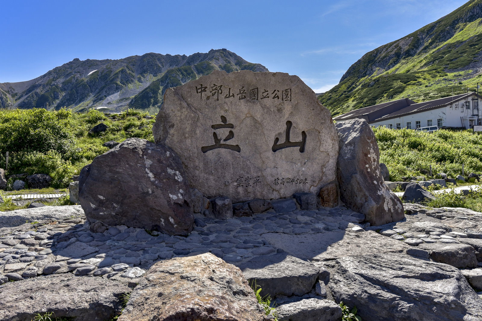 青空と緑の山々を背景に立つ立山の石碑