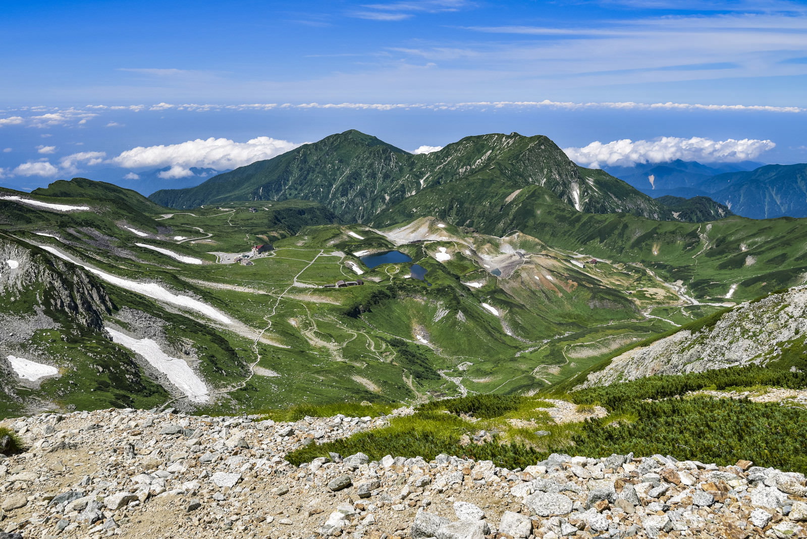 青空の下に広がる立山室堂の山々、緑の斜面に残雪が見える雄大な景観