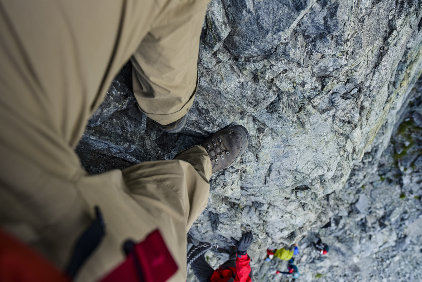 剱岳の岩壁に足をかけて登る登山者の足元と手のクローズアップ