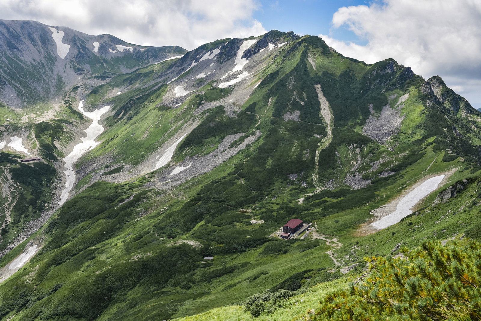 剱岳別山尾根から望む剣山荘方面の山岳風景、緑の山肌と残雪