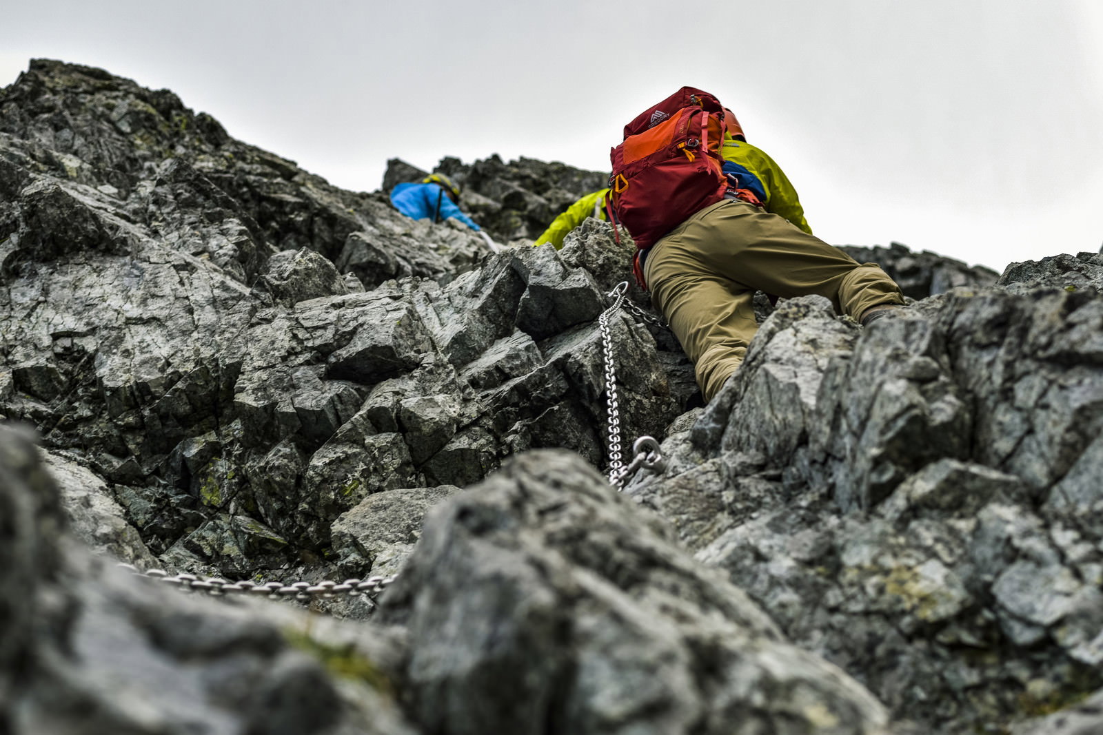 赤いザックを背負った登山者が灰色の険しい岩壁を登っている様子