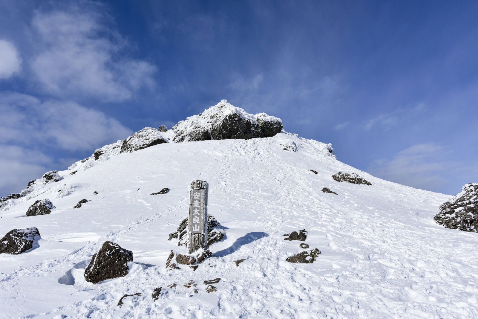 雪に覆われた安達太良山の山頂に立つ山頂標と青空