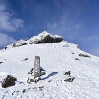 冬の安達太良山山頂に立つ山頂標と青空の写真
