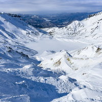午後の光が差す安達太良山の爆裂火口と雪に覆われた冬の火口壁の写真